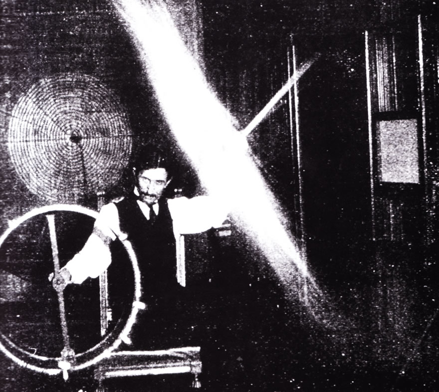 Tesla at his Houston street laboratory in 1898, sending 500,000 volts through his body to light a wireless fluorescent light. Image source Wiki commons.